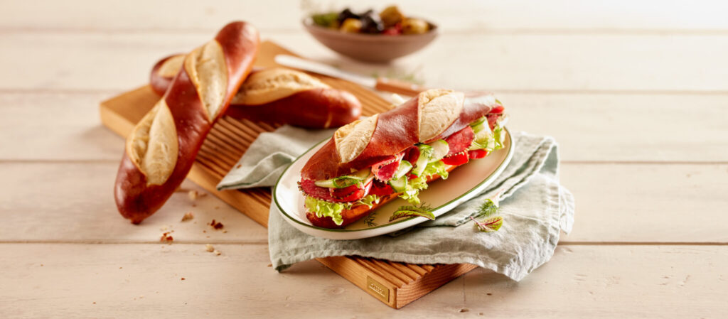Pretzel Baguette Filled with lettuce, Meat, and tomato served on a plate